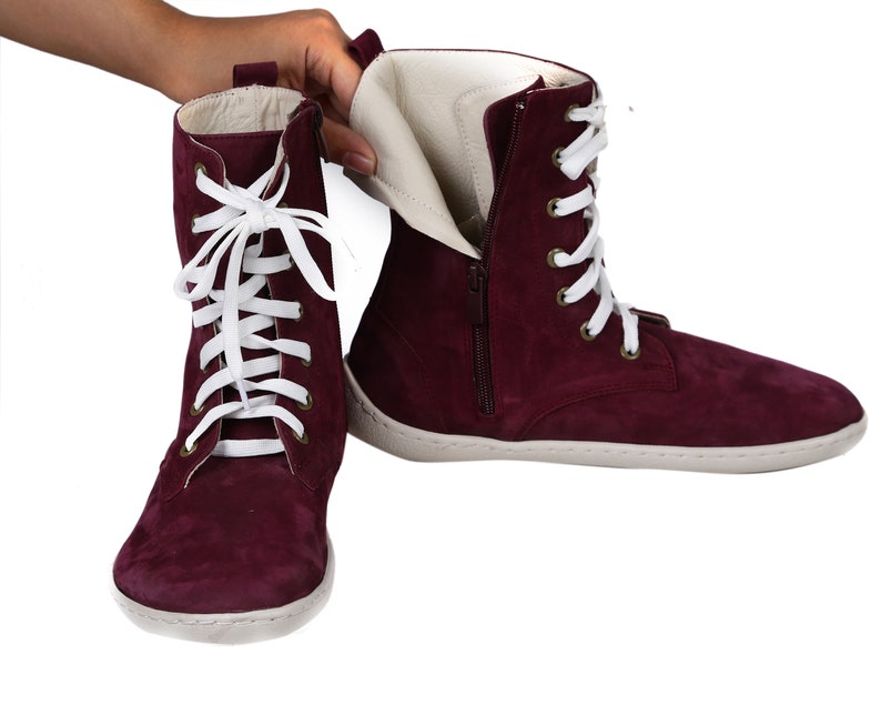 May include: Burgundy suede ankle boots with white laces and a zipper on the side. The boots have a white rubber sole.