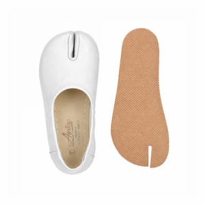 May include: White split-toe shoe with a separate brown sole. The shoe has a rounded toe with a split for the big toe. The sole is a light brown color with a textured surface. The shoe is made of a smooth, white material.