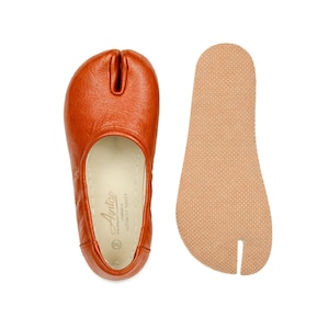 May include: Orange leather split-toe ballet flats with a separate beige insole. The flats have a rounded toe and a split between the big toe and the other toes. The insole is textured. The brand name "Antap" is visible on the shoe.