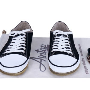 May include: Two black canvas sneakers with white laces and white soles. The shoes are sitting on a beige canvas bag with the word 'Ainto' printed on it. The bag also has the text 'aintnoprefootfeel' and 'www.ainttop.com' printed on it.