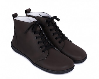 Peut inclure: Une paire de bottines marron foncé avec une finition mate lisse, des lacets noirs passés dans des œillets métalliques noirs, un bout arrondi, une languette au talon et une semelle noire plate avec une doublure intérieure blanche visible au col.