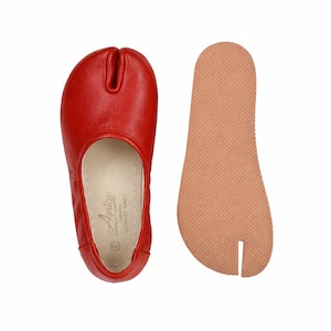 May include: A pair of red leather split-toe shoes, with a separate tan-colored sole. The shoes have a distinctive design with a space for the big toe. The sole is textured. The shoes are labeled "Antap" and "Made in Gaziantep Turkey".