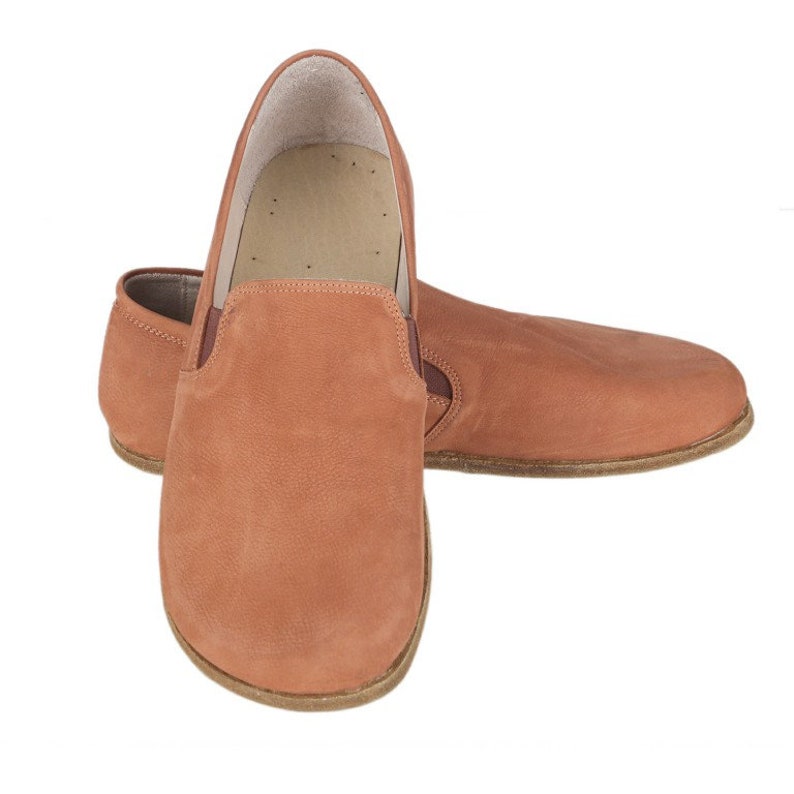 Pu&ograve; includere: Un paio di scarpe da uomo in pelle marrone con finitura in camoscio. Le scarpe hanno una punta arrotondata e una suola piatta.
