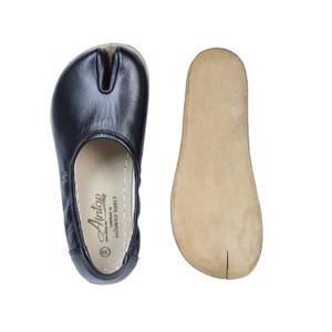 Op de afbeelding: Zwarte leren schoen met splitteen en bijpassende leren binnenzool. De schoen heeft een ronde neus en een split tussen de grote teen en de andere tenen. De binnenzool is lichtbruin van kleur. De schoen is gemarkeerd met "Aintap".