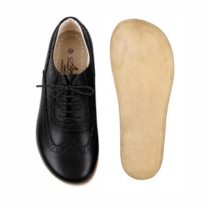 May include: A black leather oxford shoe with brogue detailing and thin black laces, shown alongside a separate light tan insole. The shoe features a rounded toe box and a size 39 label printed on the interior heel area with the brand name Air.