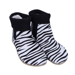 Könnte beinhalten: Ein Paar Stiefeletten mit Zebramuster. Die Stiefel haben einen schwarzen Rippstrickbund und ein weißes und schwarzes Zebramuster. Die Stiefel sind aus einem weichen Material gefertigt.