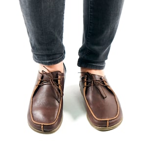 May include: A pair of brown leather lace-up shoes with a light brown trim around the sole.