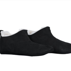 May include: A pair of black suede slippers with a white faux fur lining. The slippers have a rounded toe and a flat sole.