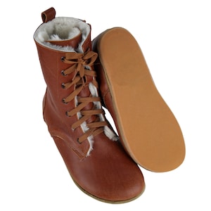 May include: Brown leather boots with a lace-up front and a white faux fur lining. The boots have a flat sole and are shown with the sole facing up.