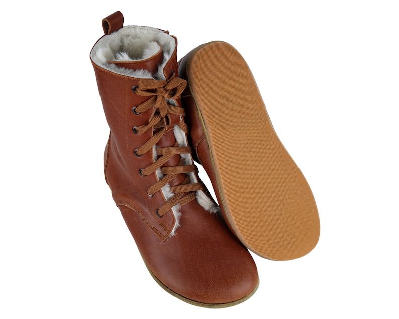 May include: Brown leather boots with a lace-up front and a white faux fur lining. The boots have a flat sole and are shown with the sole facing up.