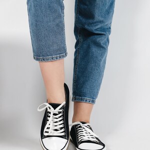 May include: Black canvas sneakers with white laces and white soles. The sneakers are worn with blue jeans.