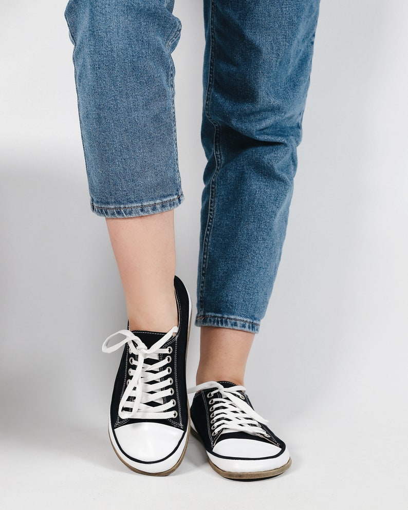 May include: Black canvas sneakers with white laces and white soles. The sneakers are worn with blue jeans.