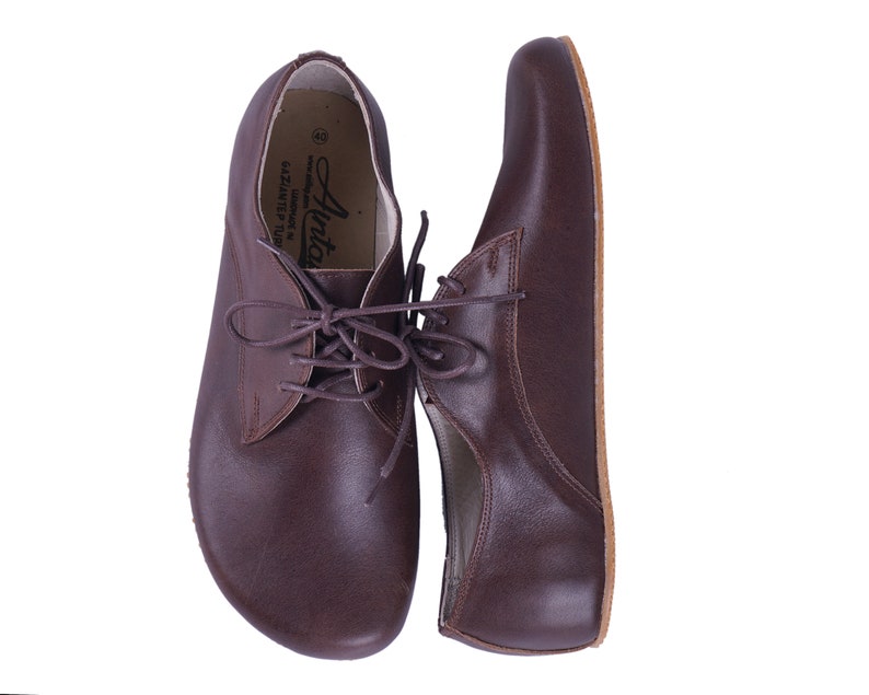 K&ouml;nnte beinhalten: Ein Paar braune Lederschn&uuml;rschuhe mit abgerundeter Spitze. Die Schuhe haben ein schlichtes Design und sind aus hochwertigem Leder gefertigt.