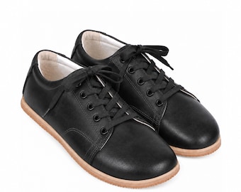 May include: A pair of black low-top sneakers featuring a smooth matte finish, black laces, black metal eyelets, and a light tan gum rubber sole. The interior lining is a light cream color, and the shoes have a rounded toe and a lace-up closure.