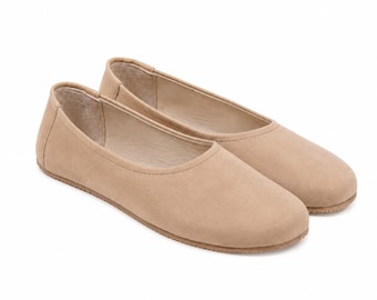 Puede incluir: Un par de zapatos planos sin cordones de color beige con punta redondeada, abertura baja y suela plana. El exterior tiene un acabado liso y mate, mientras que el forro interior es de un tono beige más claro. El diseño es sencillo y liso.