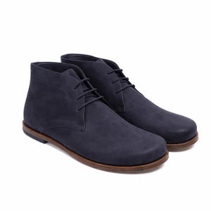 May include: A pair of navy blue chukka boots with brown soles and matching laces. The boots have a smooth, matte finish and a classic, ankle-high design. The soles are approximately 1 inch thick.