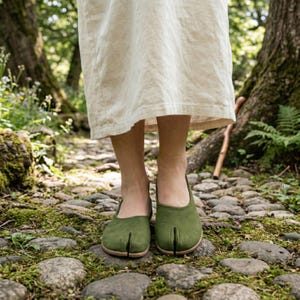 Op de afbeelding: Een paar olijfgroene schoenen met split-teen. De schoenen zijn gemaakt van een zacht materiaal en hebben een afgeronde neus. De schoenen worden gedragen op een geplaveide weg.