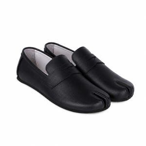 May include: A pair of black leather loafers featuring a distinctive split-toe design at the front. These slip-on shoes have a smooth matte finish, a wide strap across the vamp, and a white interior lining, showcasing a low-profile silhouette.