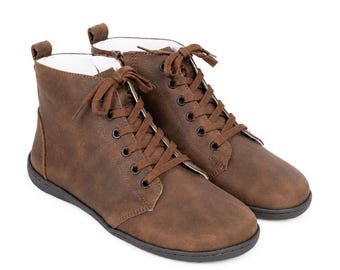 May include: A pair of brown ankle boots featuring a smooth, matte finish, matching brown laces threaded through five pairs of dark metal eyelets, a rounded toe, a pull tab at the heel, and a thin, flexible black sole with a white interior lining.