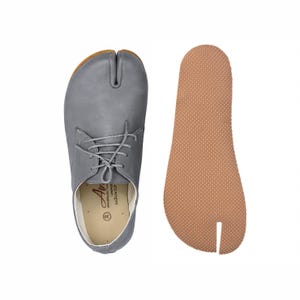 Op de afbeelding: Grijze leren schoen met split-teen en veters, naast een bijpassende binnenzool. De schoen heeft een bruine zool en een split-teenontwerp. De binnenzool is lichtbruin van kleur. Maat 38.