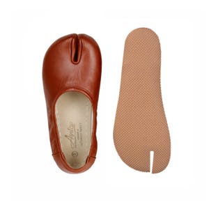 May include: A pair of brown leather split-toe shoes, with a separate sole. The shoe has a rounded toe with a split for the big toe. The sole is a light brown color with a textured surface. The shoe is labeled "Antap".
