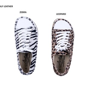 May include: A pair of white canvas sneakers with black and white zebra print and brown and black leopard print. The sneakers have white laces and a white rubber sole. The text "Avitcae" is printed on the inside of the sneakers.