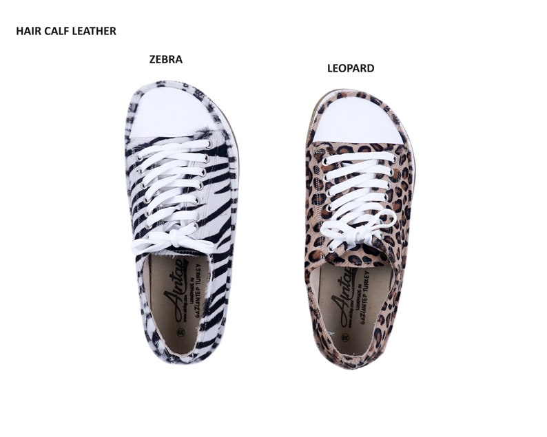 May include: A pair of white canvas sneakers with black and white zebra print and brown and black leopard print. The sneakers have white laces and a white rubber sole. The text "Avitcae" is printed on the inside of the sneakers.