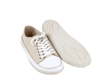 May include: A pair of beige leather low-top sneakers with white laces and a white rubber sole. The insole is also visible, showing a beige rubber material with a textured pattern.