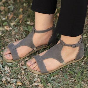 Puede incluir: Un par de sandalias de cuero gris con hebillas. Las sandalias tienen un dise&ntilde;o de correa en T y se usan en los pies.