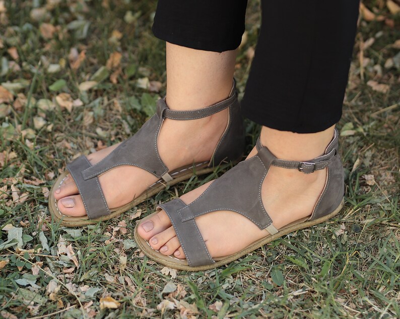 Puede incluir: Un par de sandalias de cuero gris con hebillas. Las sandalias tienen un dise&ntilde;o de correa en T y se usan en los pies.