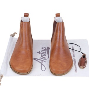 May include: A pair of brown leather ankle boots with elastic side panels and a pull-on tab. The boots are on a white surface with the word "Aimtap" written in black.
