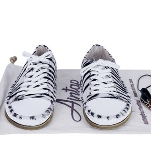 May include: A pair of white and black zebra print sneakers with white laces. The sneakers are on a white canvas bag with the word "Ainto" printed on it.