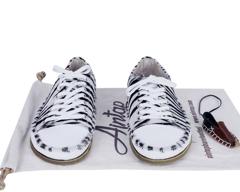May include: A pair of white and black zebra print sneakers with white laces. The sneakers are on a white canvas bag with the word "Ainto" printed on it.