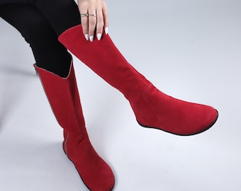 May include: A pair of red suede knee-high boots with a pointed toe and a low heel.