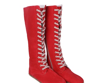 Puede incluir: Un par de botas rojas hasta la rodilla con cordones blancos. Las botas tienen suela plana y cremallera lateral. Los cordones suben por la parte delantera de las botas, creando un look clásico y elegante. Las botas son de material suave.