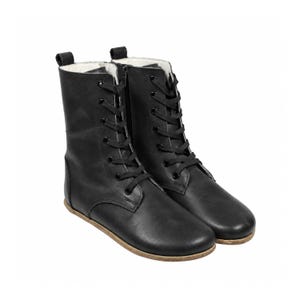 May include: A pair of black mid-calf boots featuring a lace-up front with black eyelets and black laces. The boots have a side zipper closure, a rounded toe, and a light-colored interior lining, set upon a thin, flat, light-brown sole.