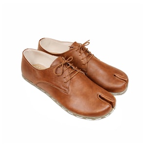 May include: A pair of brown leather split-toe shoes with laces. The shoes have a unique design with a separate compartment for the big toe. The soles are a light color.