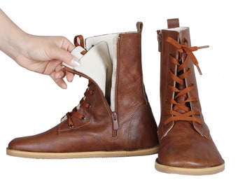 May include: A pair of brown leather ankle boots featuring a side zipper, brown laces, and a light-colored interior lining. The boots have a flat sole and a pull tab at the back of the heel. One boot is shown from the side and one from the front.