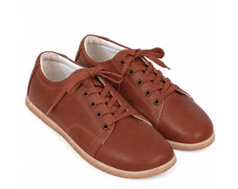 May include: A pair of low-top sneakers in a solid brown color. These shoes feature a smooth exterior, matching brown laces threaded through metal eyelets, a rounded toe box, and a light-colored, textured rubber sole with a white interior lining.