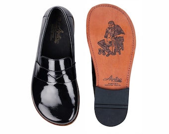 May include: Black patent leather loafers with a glossy finish, displayed next to a shoe sole with a brown leather insole. The insole features a detailed illustration of a shoemaker and the brand name "Antap".