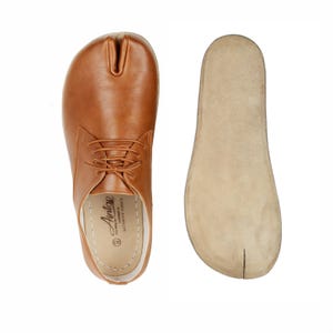 Op de afbeelding: Een paar bruin lederen schoenen met split-teen en veters, en een aparte binnenzool. De schoenen hebben een uniek ontwerp met een split tussen de grote teen en andere tenen. De binnenzool is beige. Maat 42.