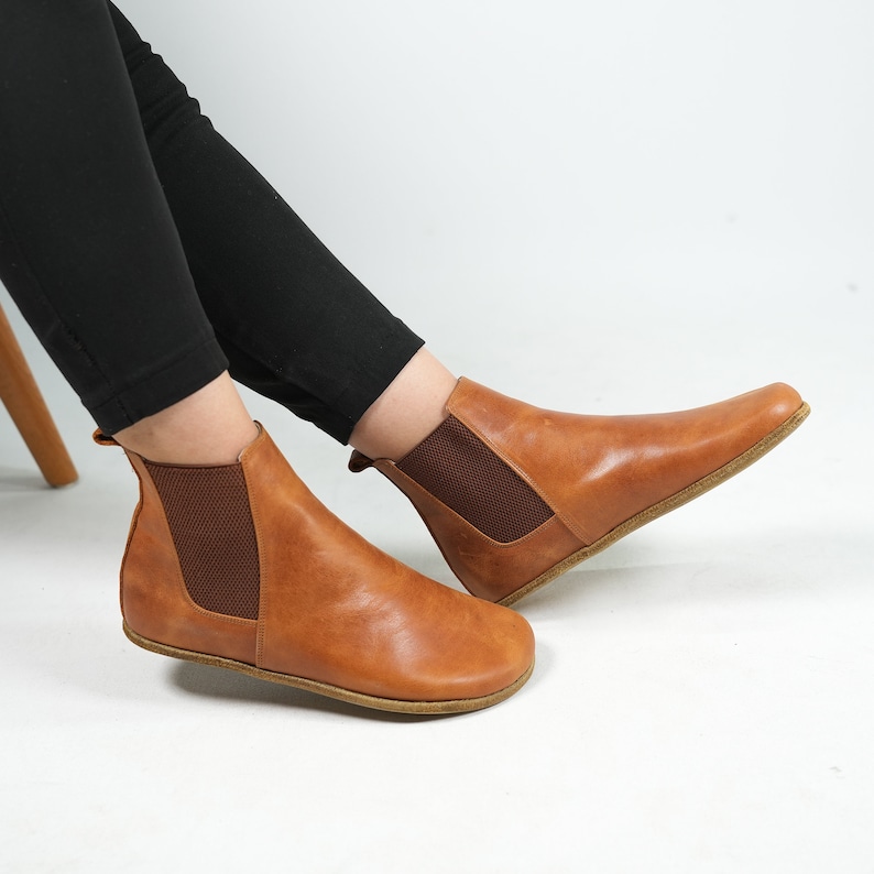 May include: A pair of brown leather ankle boots with elastic side panels. The boots have a rounded toe and a flat sole.