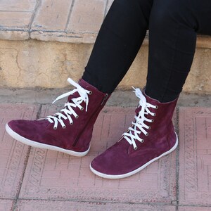 May include: Burgundy suede high-top boots with white laces and a zipper on the side.