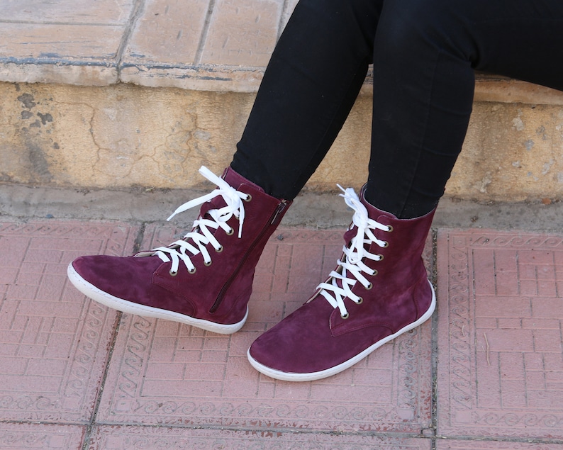 May include: Burgundy suede high-top boots with white laces and a zipper on the side.