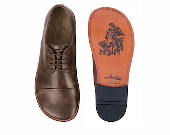 Könnte beinhalten: Braune Lederschuhe mit Schnürsenkeln, neben einer Schuhsohle mit einer Handwerker-Illustration. Die Sohle trägt den Markennamen "Airtap" und den Schriftzug "Handmade in Gaziantep, Türkiye".