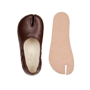 May include: A pair of brown leather split-toe shoes with a matching insole. The shoes have a unique design with a separate section for the big toe. The insole is a light tan color and has a textured surface. The shoes are designed for comfort and style.