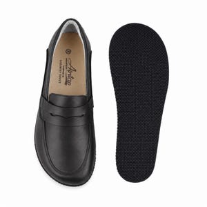 May include: A black leather penny loafer shoe with a smooth upper and a strap across the vamp. The interior insole features the text Aintap, Handmade in Gaziantep Turkey, and the size 39. Beside it is a separate black textured rubber outsole.