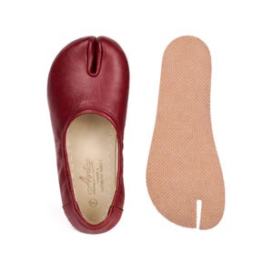 May include: A pair of burgundy leather split-toe shoes with a separate beige insole. The shoes have a unique design with a split between the big toe and the other toes. The insole is textured for grip. The shoes are labeled "Aintap" and "Made in Turkey".