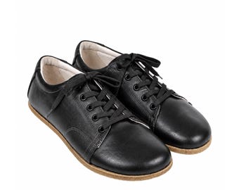 Peut inclure: Une paire de baskets basses noires avec une finition lisse, des lacets noirs, des œillets métalliques et une semelle texturée marron clair. La doublure intérieure est de couleur crème et les chaussures ont un bout arrondi avec des coutures.