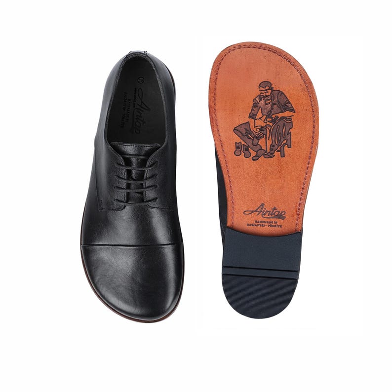 May include: Black leather dress shoe with a lace-up design, next to a shoe sole with a brown leather insole. The insole features a craftsman illustration and the brand name "Aintoe". The shoe is designed for comfort and style.